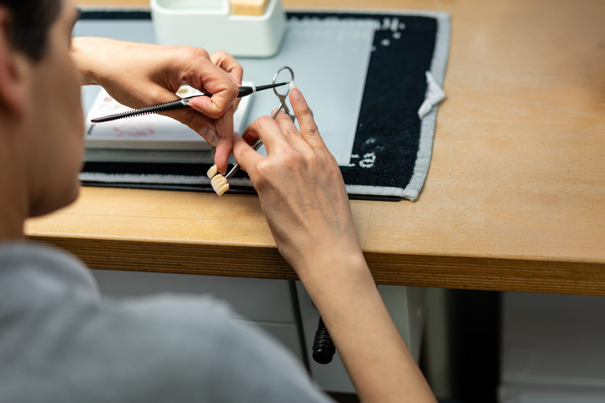Ein Mitarbeiterin sitzt im Labor um macht Feinarbeiten an einer Krone.