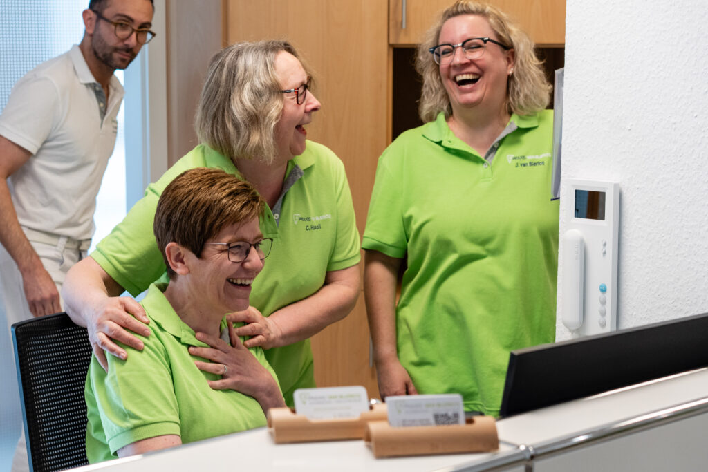 Drei Mitarbeiterinnen sitzen und stehen am Empfang und lachen.